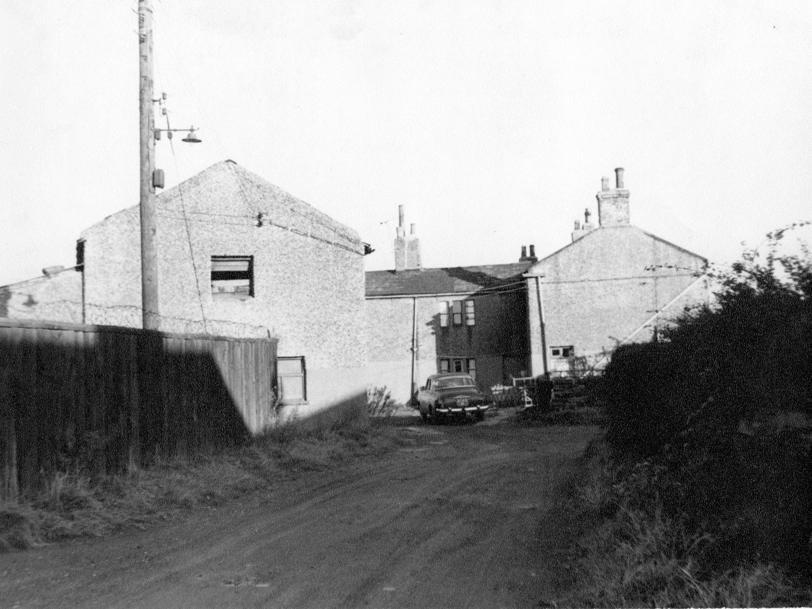 A view of unmade access road to Royal Oak Cottages. This road came from Gildersome Lane, past Moorhead woollen mill to Royal Oak. A car can be seen parked outside one of the houses.