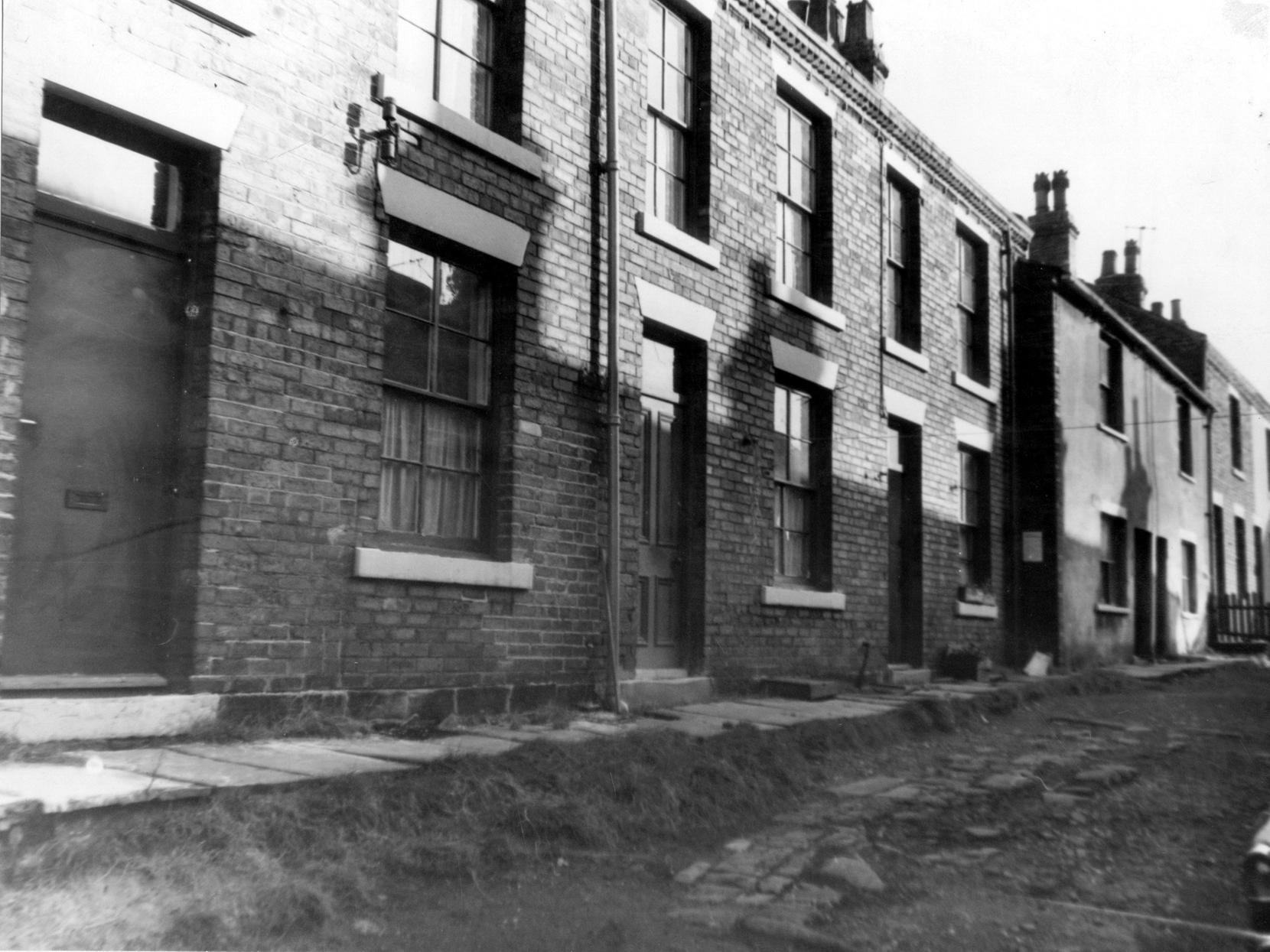 A view of terraced houses on Green Terrace. There is an unmade road in the foreground.