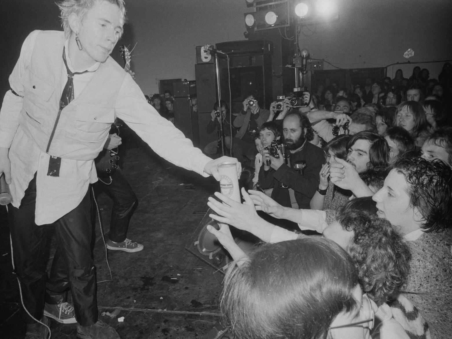 Johnny Rotten hands a can of beer to fans while on stage.