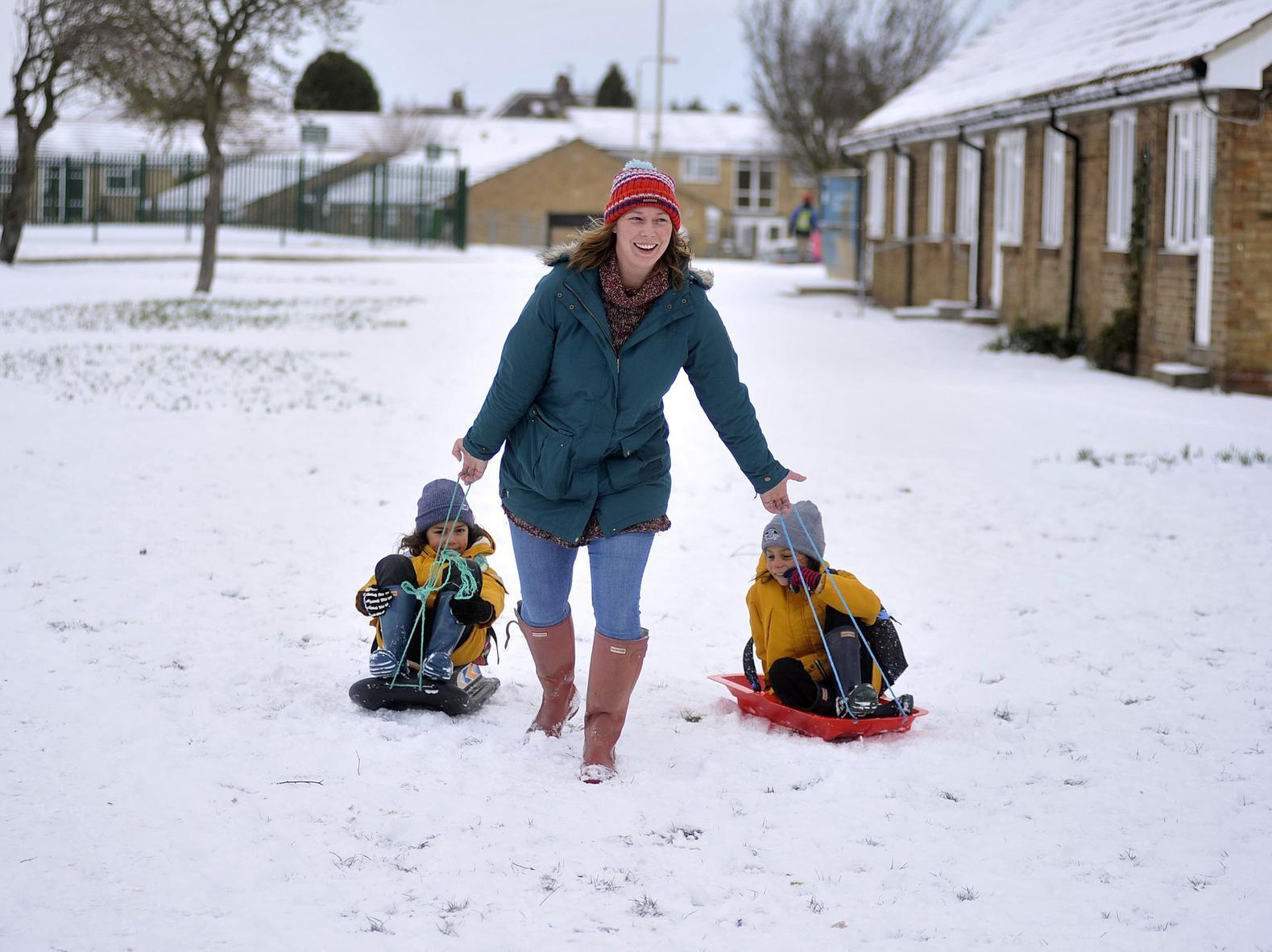 A mum takes two little ones to school on sleds.
