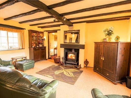 A spacious sitting room with carpet flooring and the exposed beamed ceiling, complete with log burner to keep cosy on winter nights.
