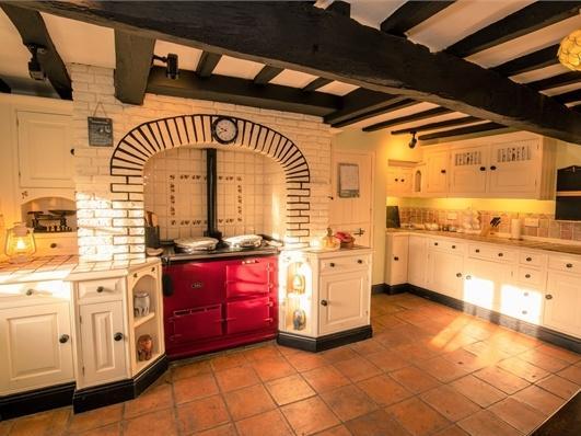 A room fitted with wall and base units with tiled worktops, an integrated Aga with a feature brick surround and original beams.