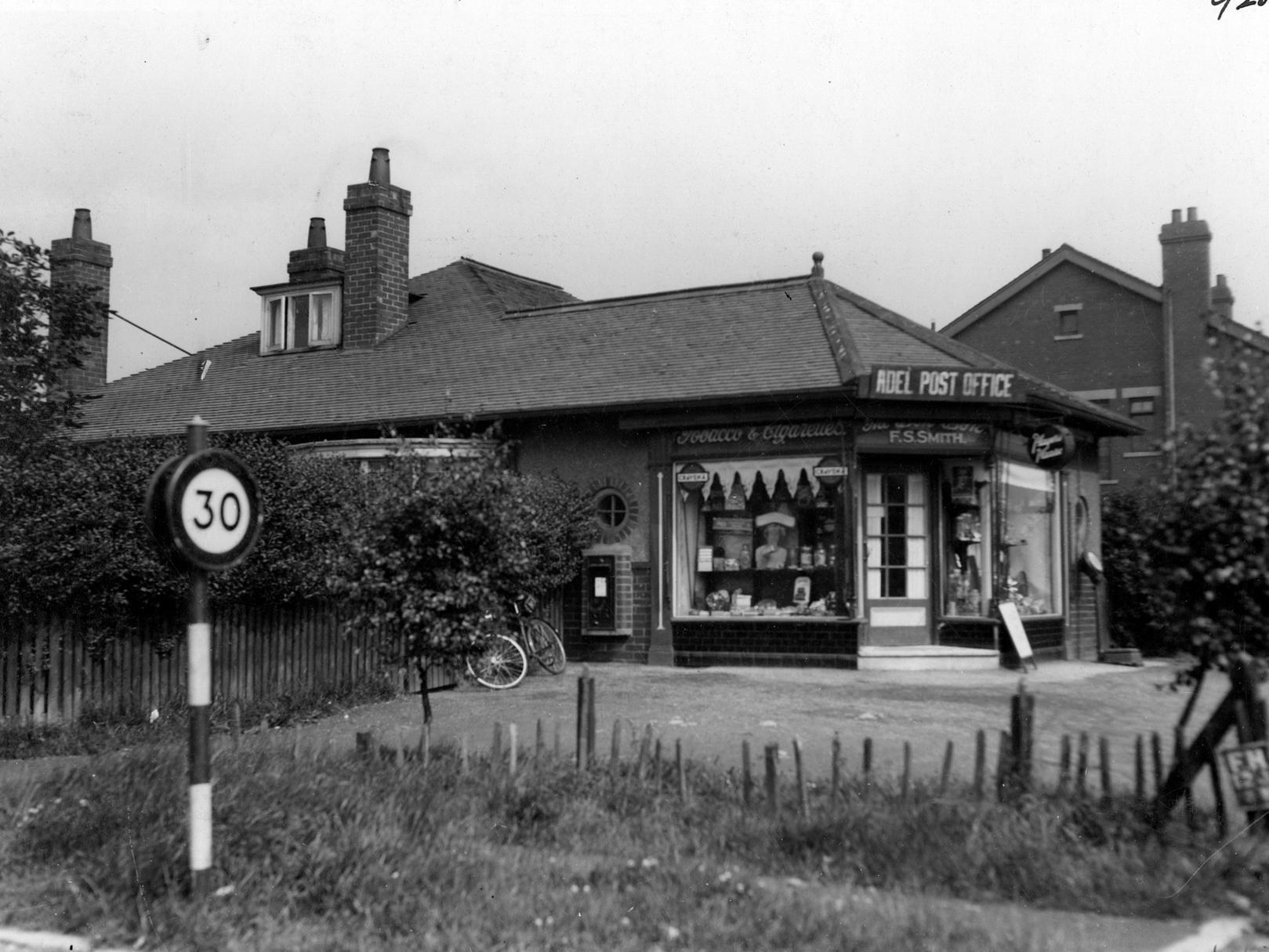 Adel Post Office on Otley Road. A post box is on the left wall. A road sign for 30 mile per hour speed limit is also to the left.