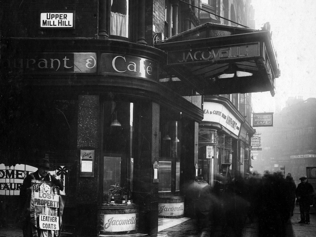 The corner of Boar Lane and Upper Mill Hill, showing Jacomelli's cafe in main view. To left of photo is a lost property man carrying leather coats.