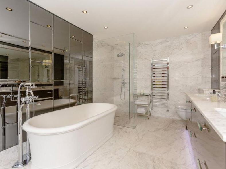 This luxurious bathroom has beautifully marble tiling, fitted sink and storage units, a stand-in shower, toilet and separate bath tub.