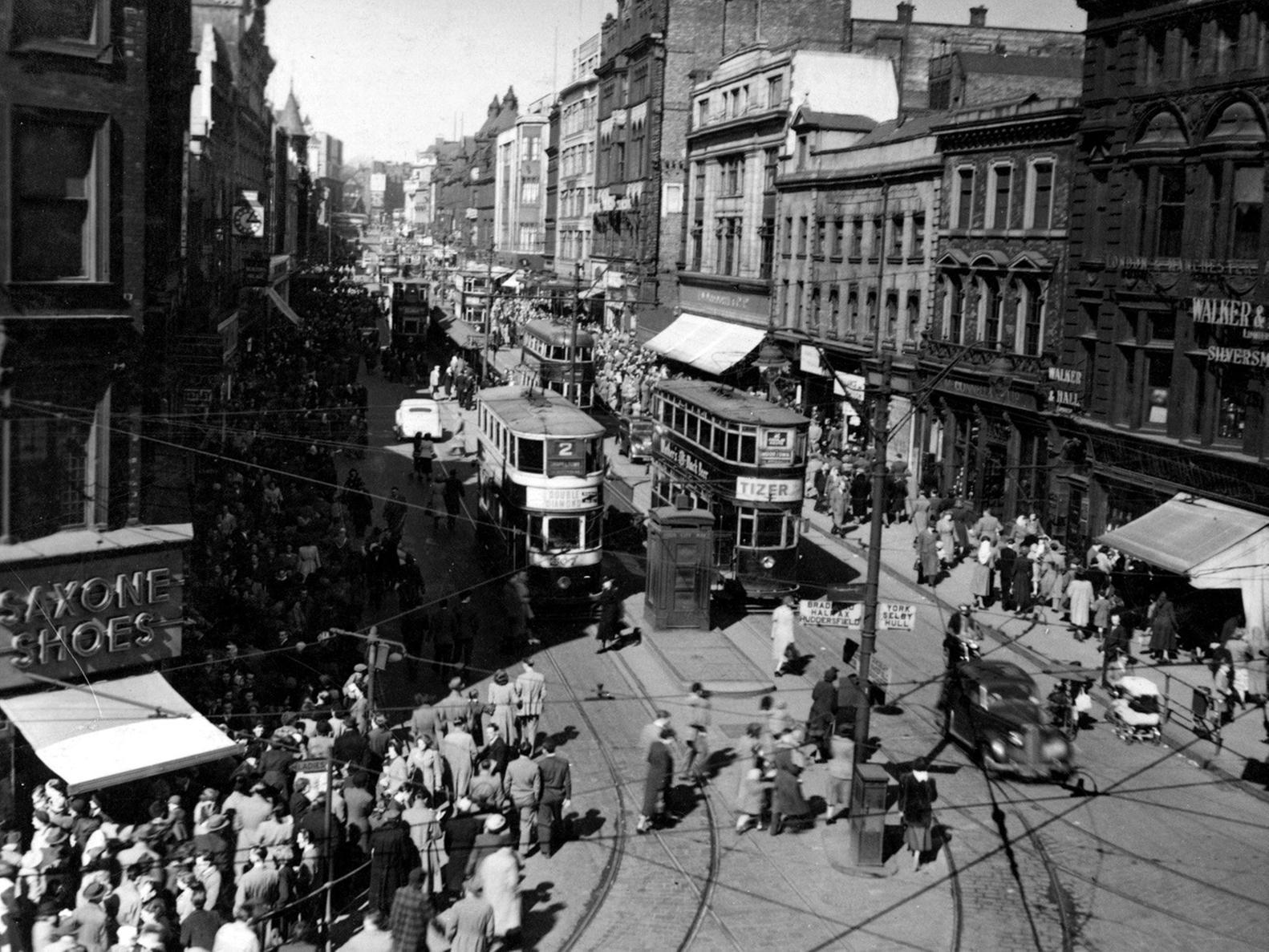 Briggate looking north from Boar Lane. At the bottom left can be seen Saxone Shoes and a parade of shops. On the right is Walker & Hall, silversmiths. There are several trams travelling along Briggate, which is full of pedestrians