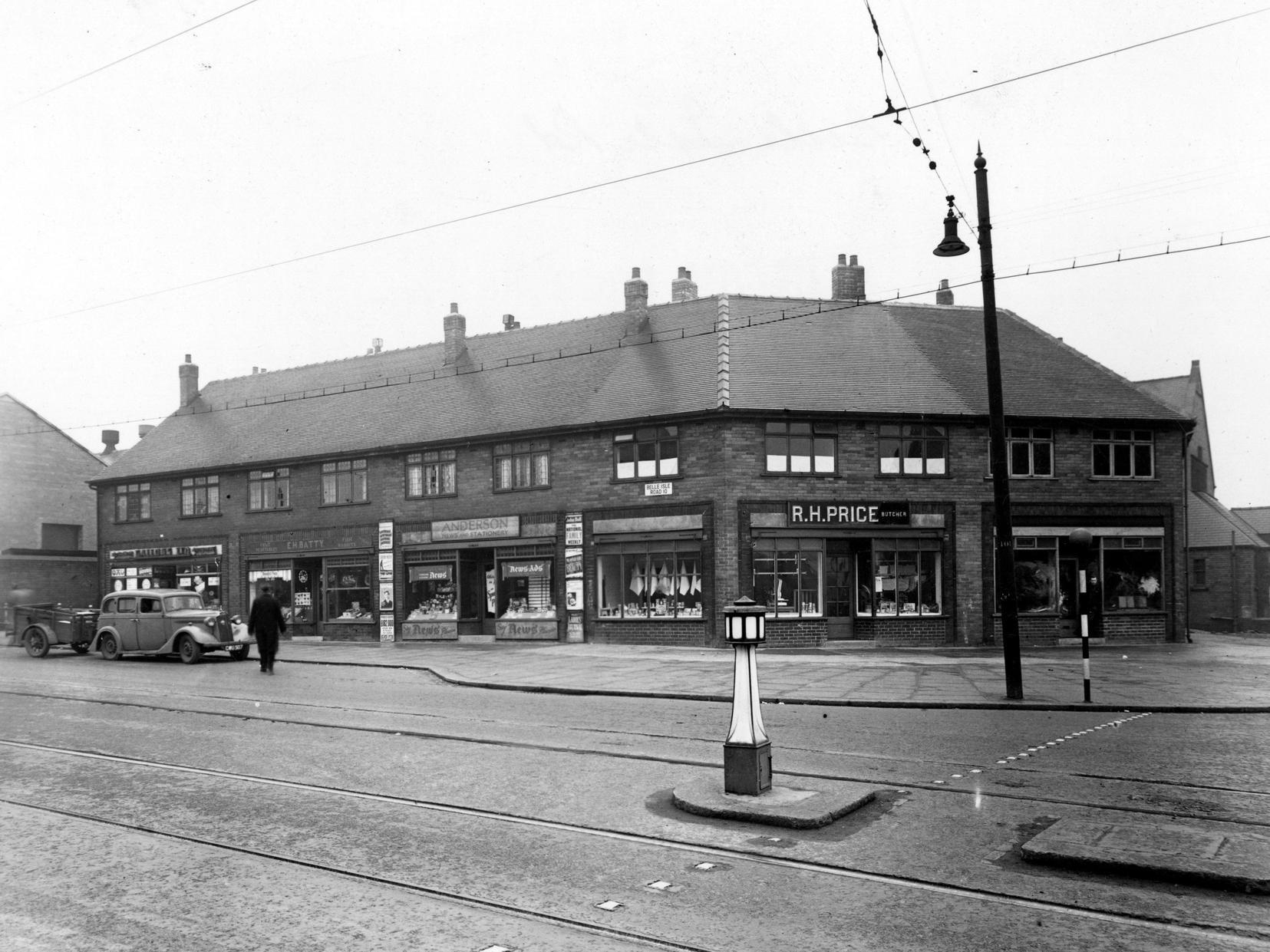 A block of shops at the corner of Belle Isle Road and Moor Road containing Gallons Ltd., a greengrocers, Andersons Newsagent and Stationers, R. H. Price Butchers and E. H. Batty's fruit and vegetables.