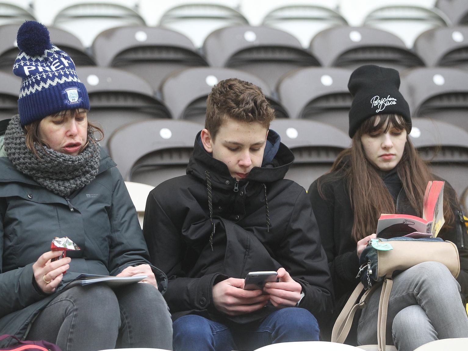 A trio of Preston fans use a different method each to keep themselves entertained as they wait for the game.