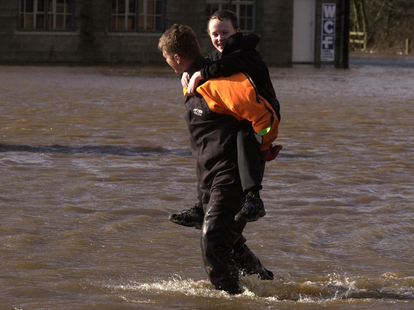 A member of the Police Underwater Search Unit carries a young boy across the flooding in Bridge Street, Otley.