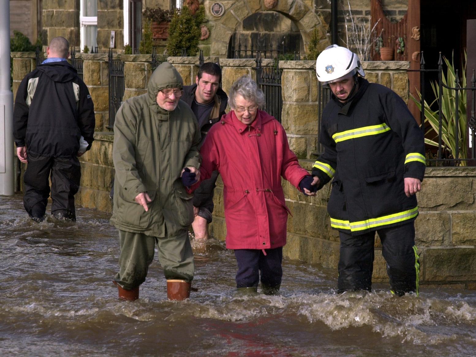A firefighter helps a couple across the floodwaters on Bridge Street, Otley.