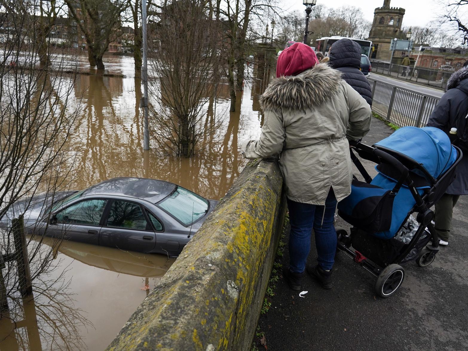 Passers by look over at an abandoned car in a flooded car park as water levels in the River Ouse in York. Photo credit: Ian Forsyth/Getty Images.