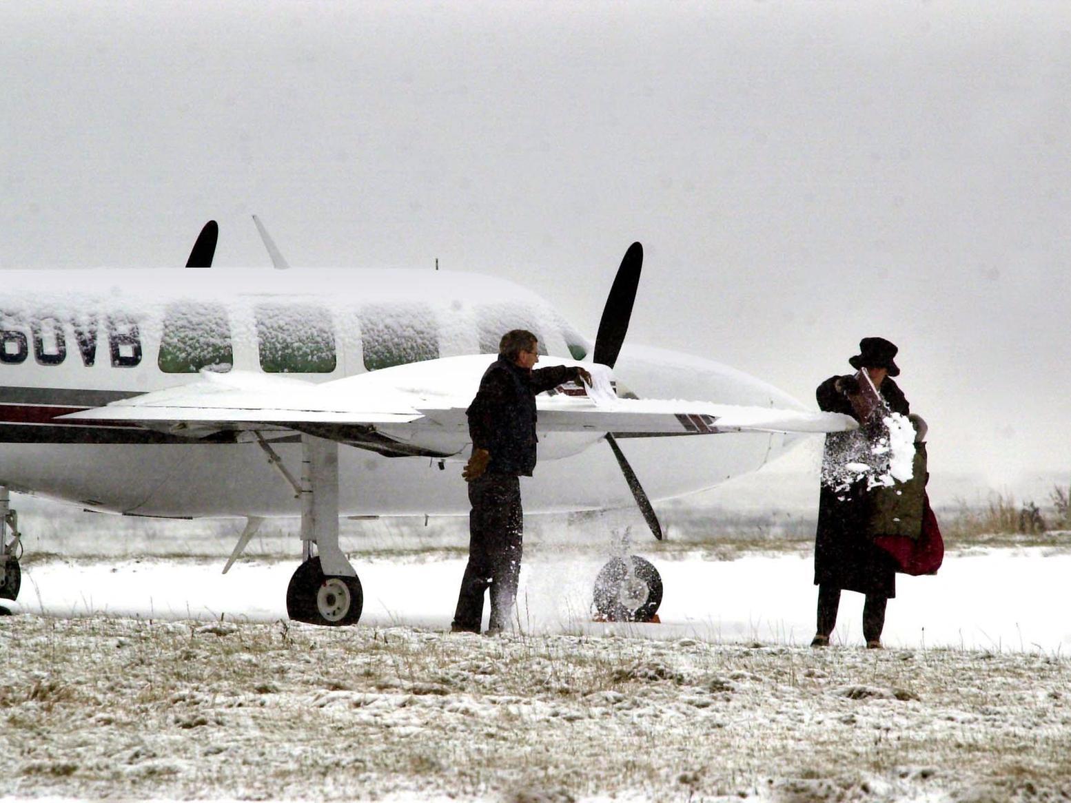 Two people brush off snow from a light aircraft, before taking to the air from Multiflight near Leeds Bradford Airport.