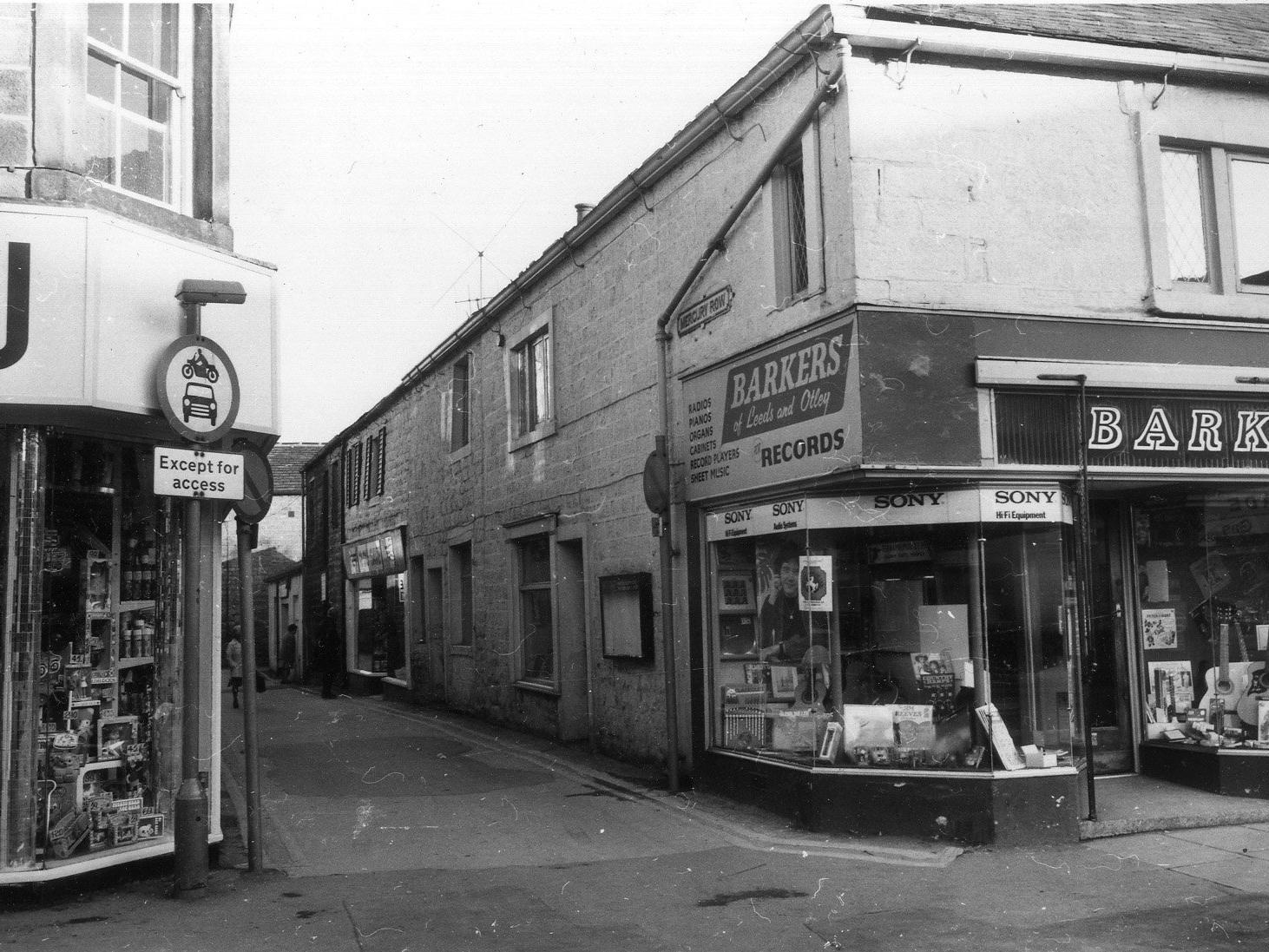 Kirkgate at the junction with Mercury Row. To the right of the junction is Barkers musical instruments and records. On the left, part of Bakers clothiers and drapers can be seen.