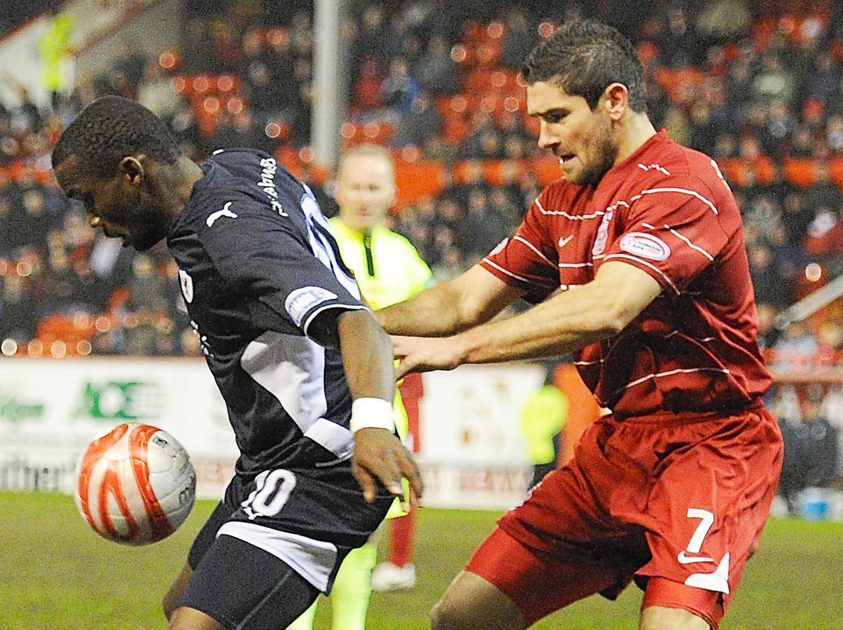 Gregory Tade is marshalled by Dons defender Jim Paterson.