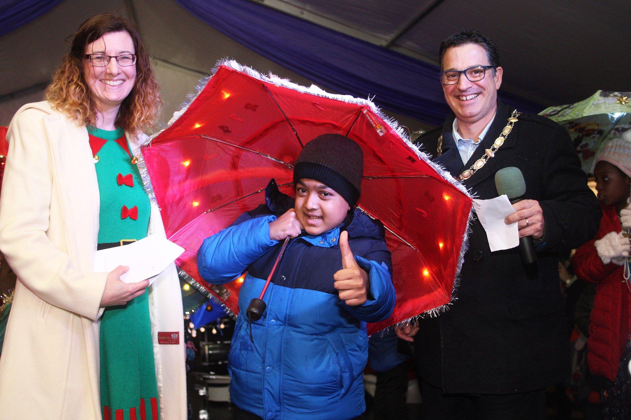 DM19112420a.jpg. Haywards Heath Christmas Lights. Illuminated umbrella competition winner Abhinav Raman with Gina Stainer from the Mid Sussex Times and the mayor Cllr Alastair McPherson. Photo by Derek Martin Photography. SUS-191123-215652008